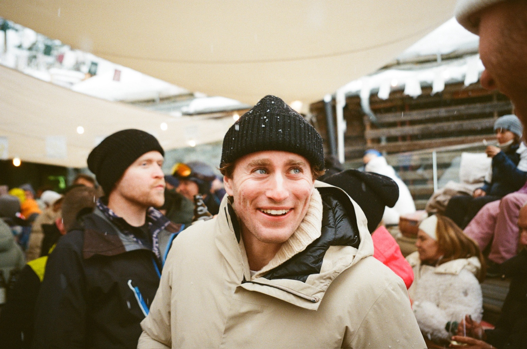 Jack Abramowich in a beanie and parka, mid-conversation at a mountain bar in falling snow