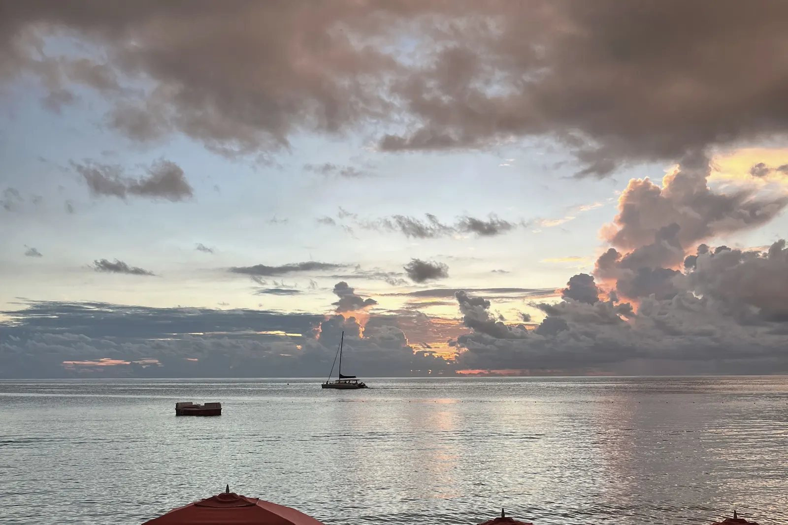 Red umbrellas on the sand at sunset, a boat anchored offshore.