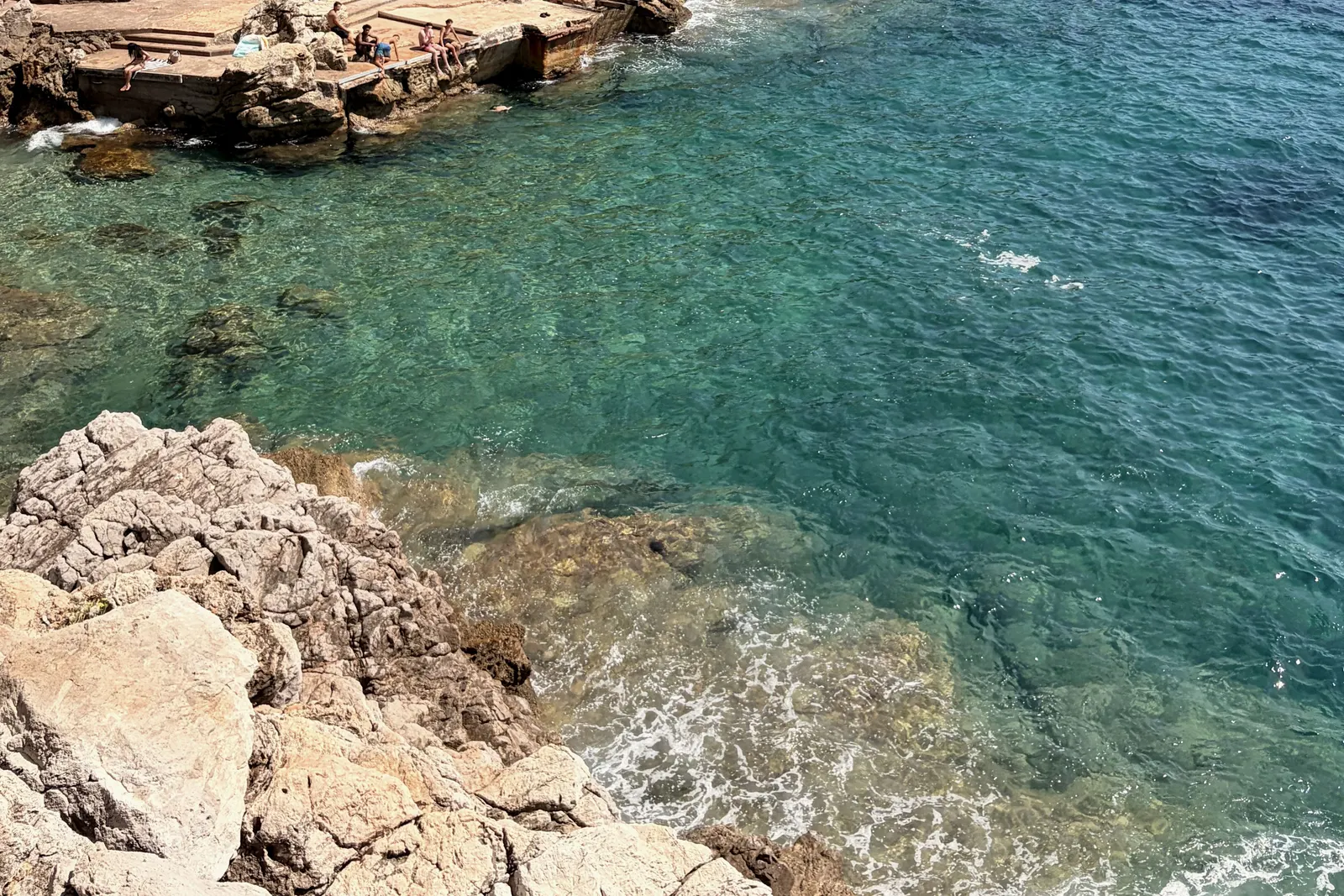 A rocky cove on the Côte d'Azur, water clear enough to read the bottom.