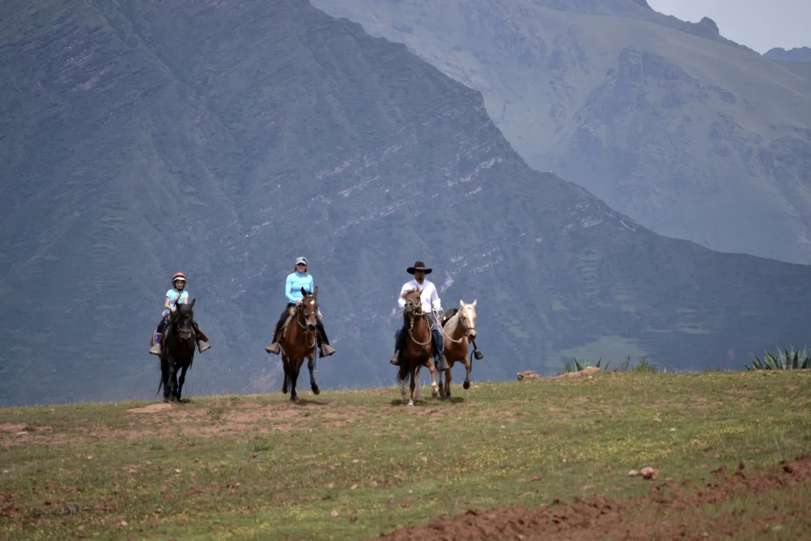Three riders on a ridge above the Sacred Valley, the far wall of the valley rising behind them.