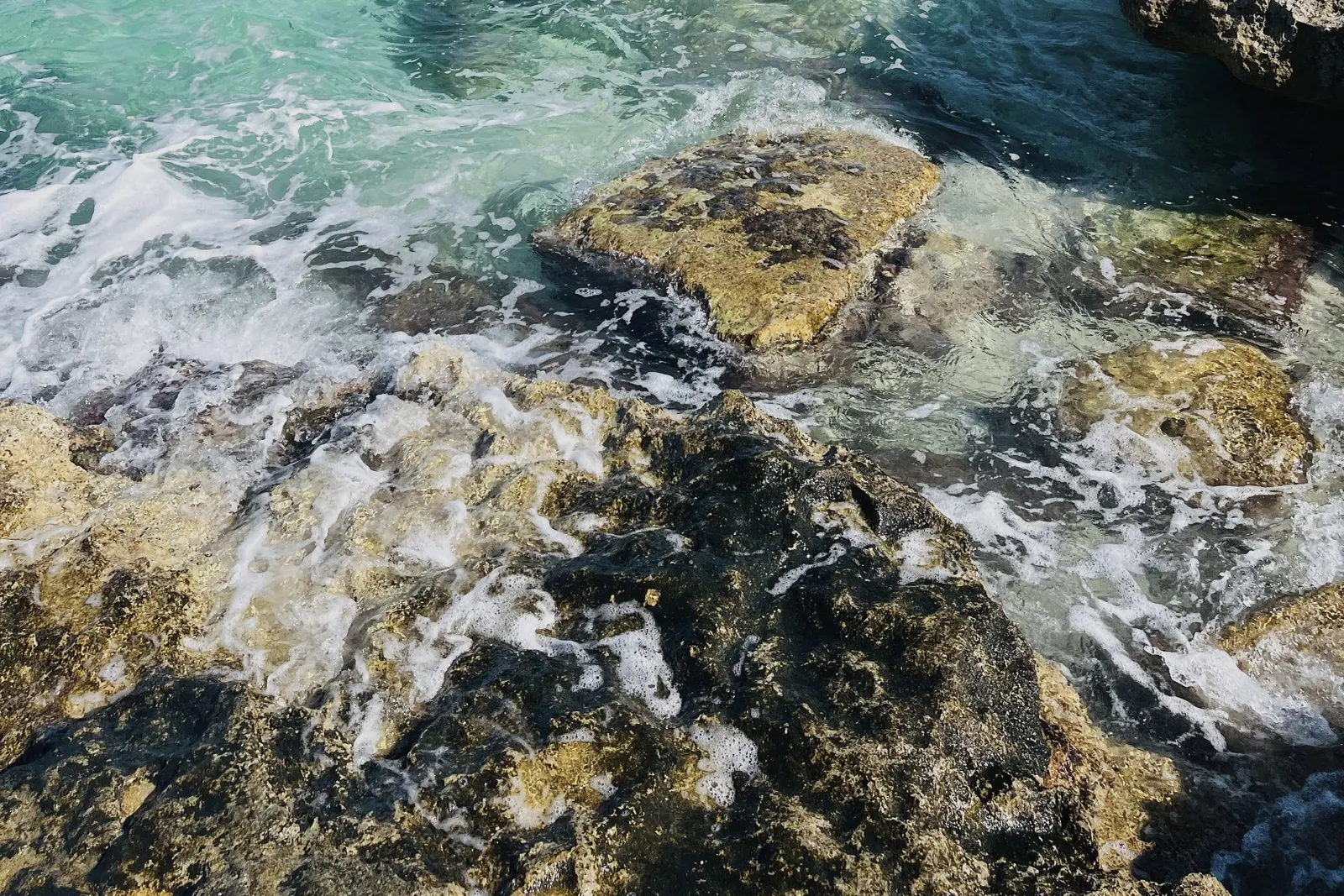 Clear water over rock on the Puglian coast, surf breaking white at the edge.