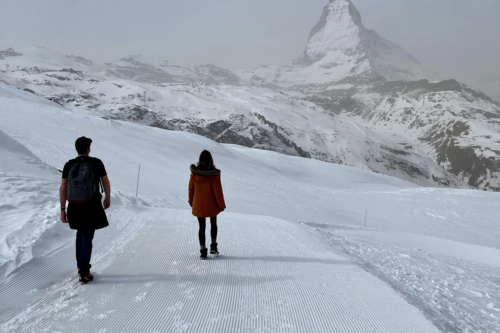 Two walkers on a groomed track above Zermatt, the Matterhorn standing at the end of it.